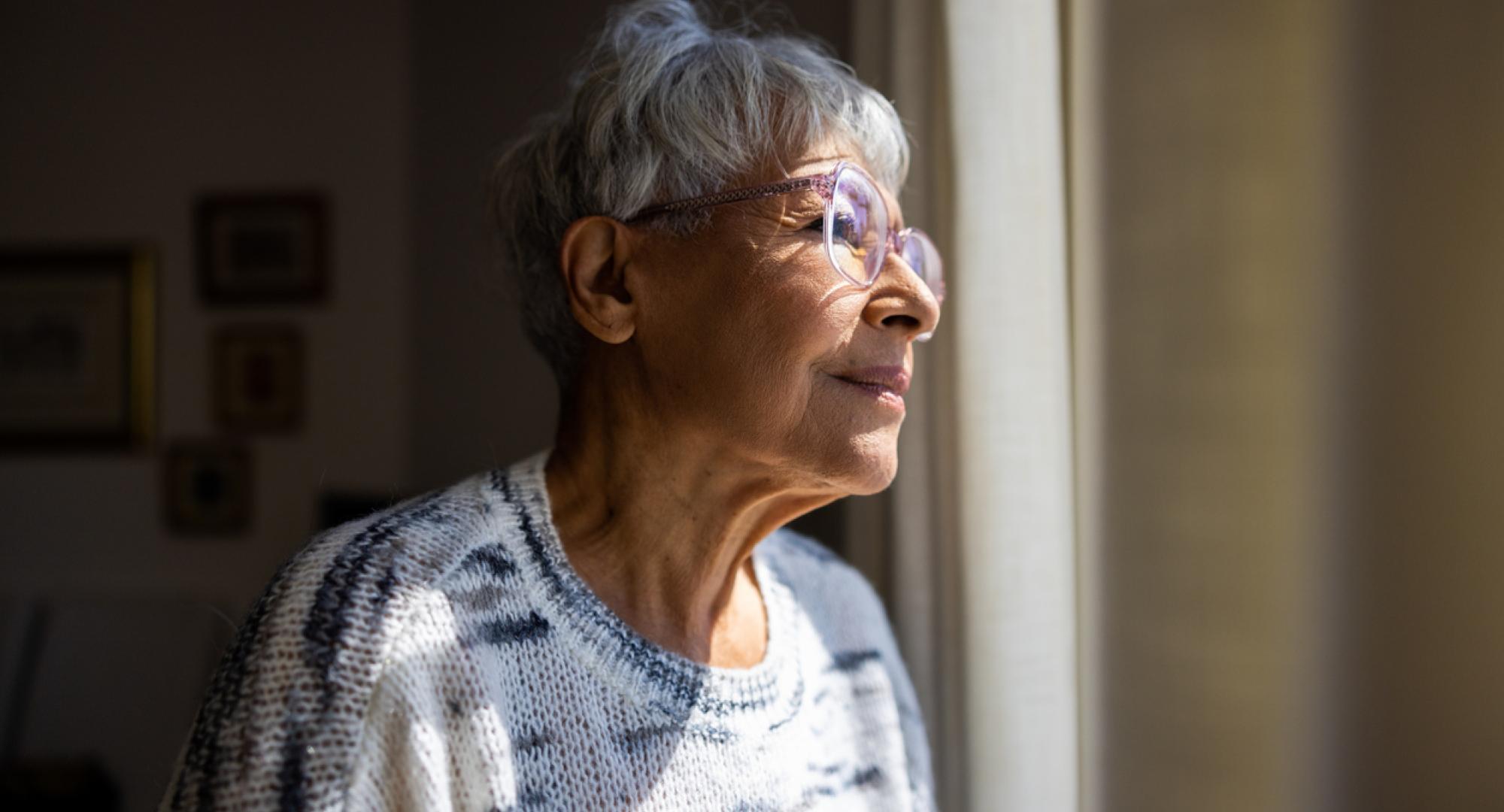 Senior woman looking out the windows of her home