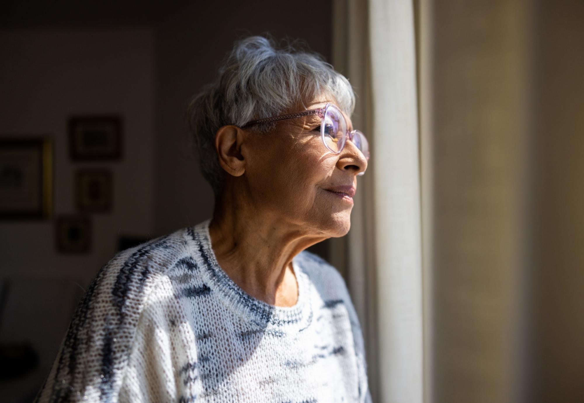 Senior woman looking out the windows of her home