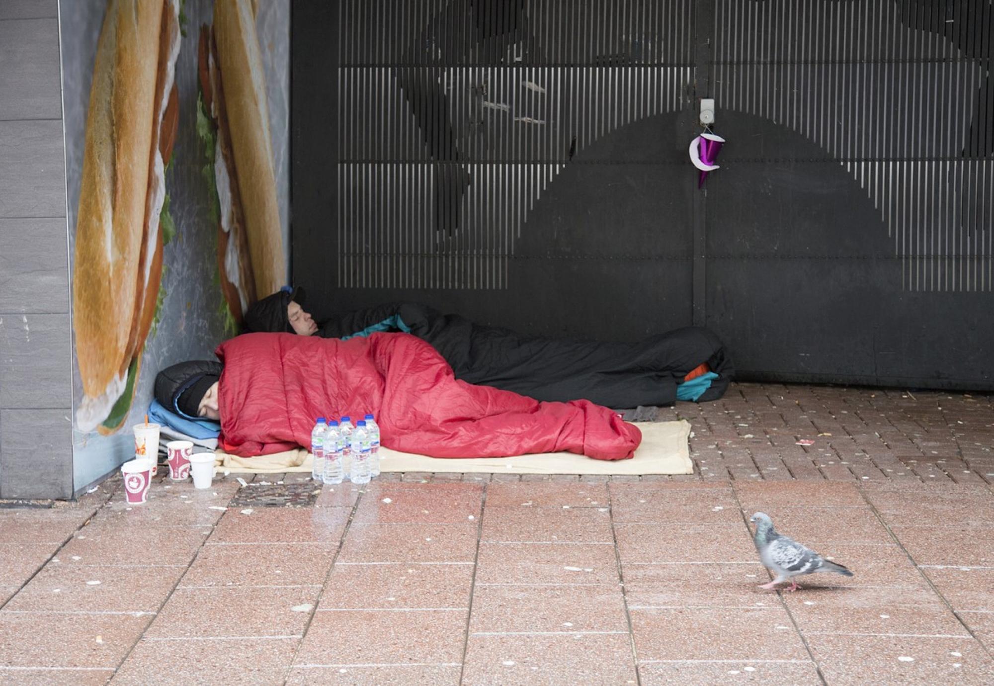 A homeless couple are sleeping in a doorway.