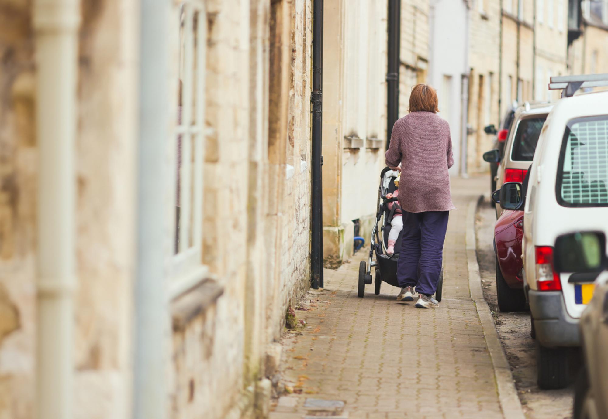 Woman pushing a child along the pavement in a pushchair