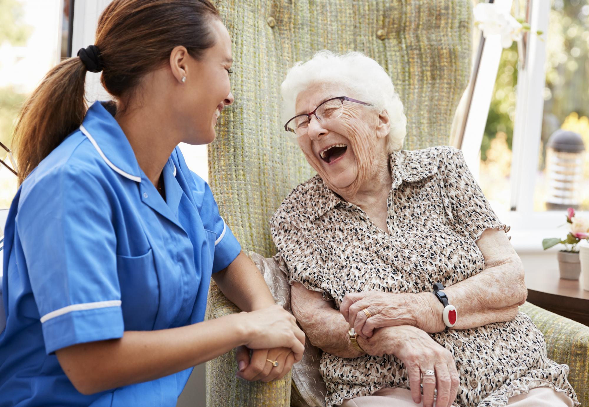 Senior Woman Sitting In Chair And Laughing With Nurse