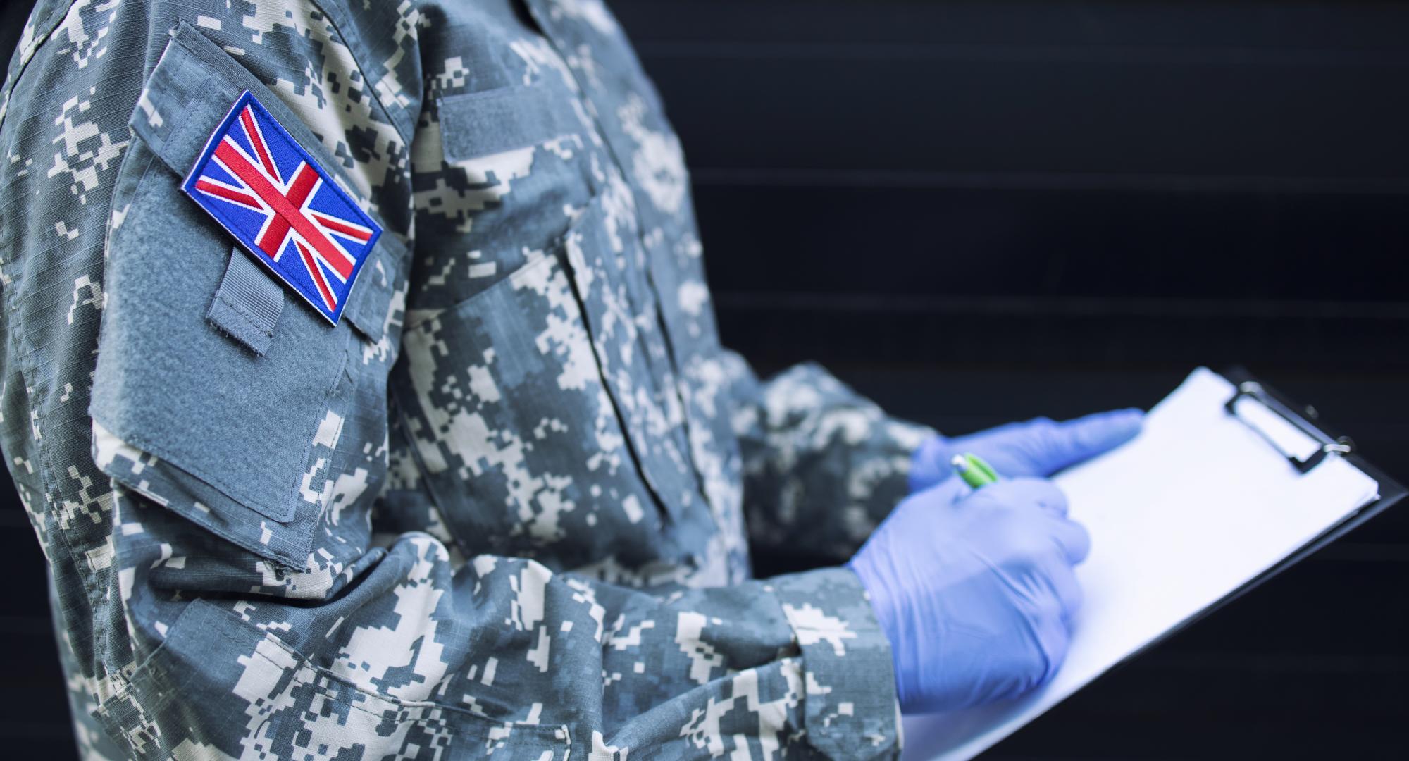 Britain soldier in camouflage uniform with rubber gloves, mask guarding in front of hospital's door controlling who gets in or out.