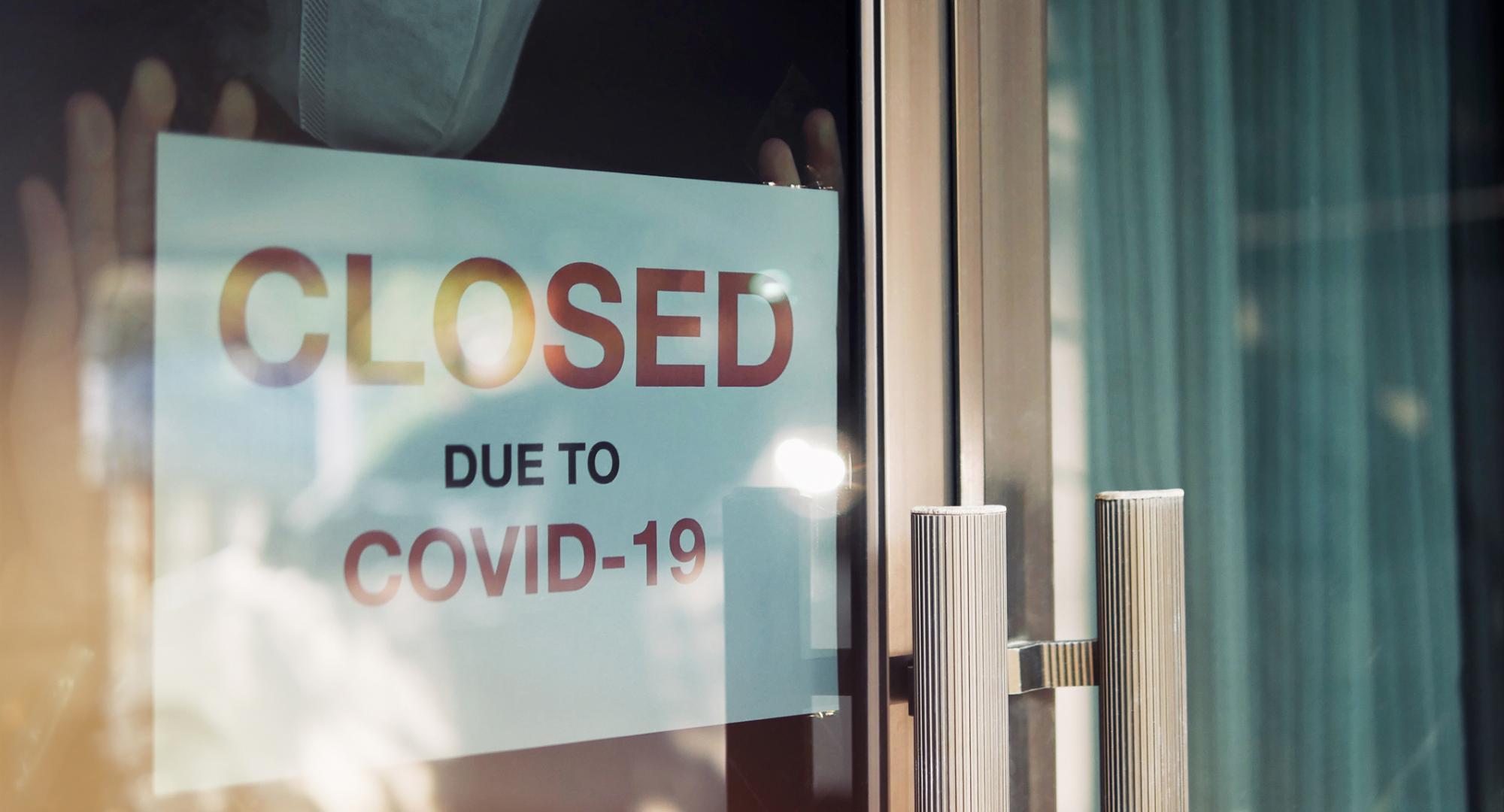 Person puts sign up that says "Closed due to Covid" in their shop window.