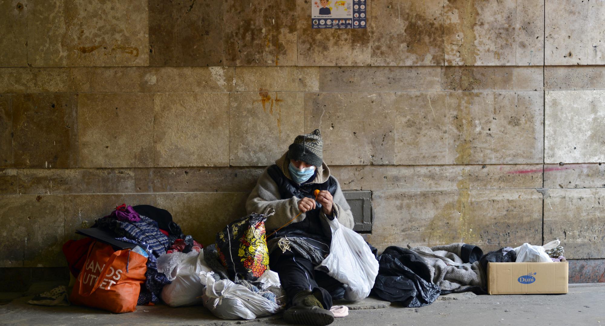 Homeless person sits against the wall in winter.