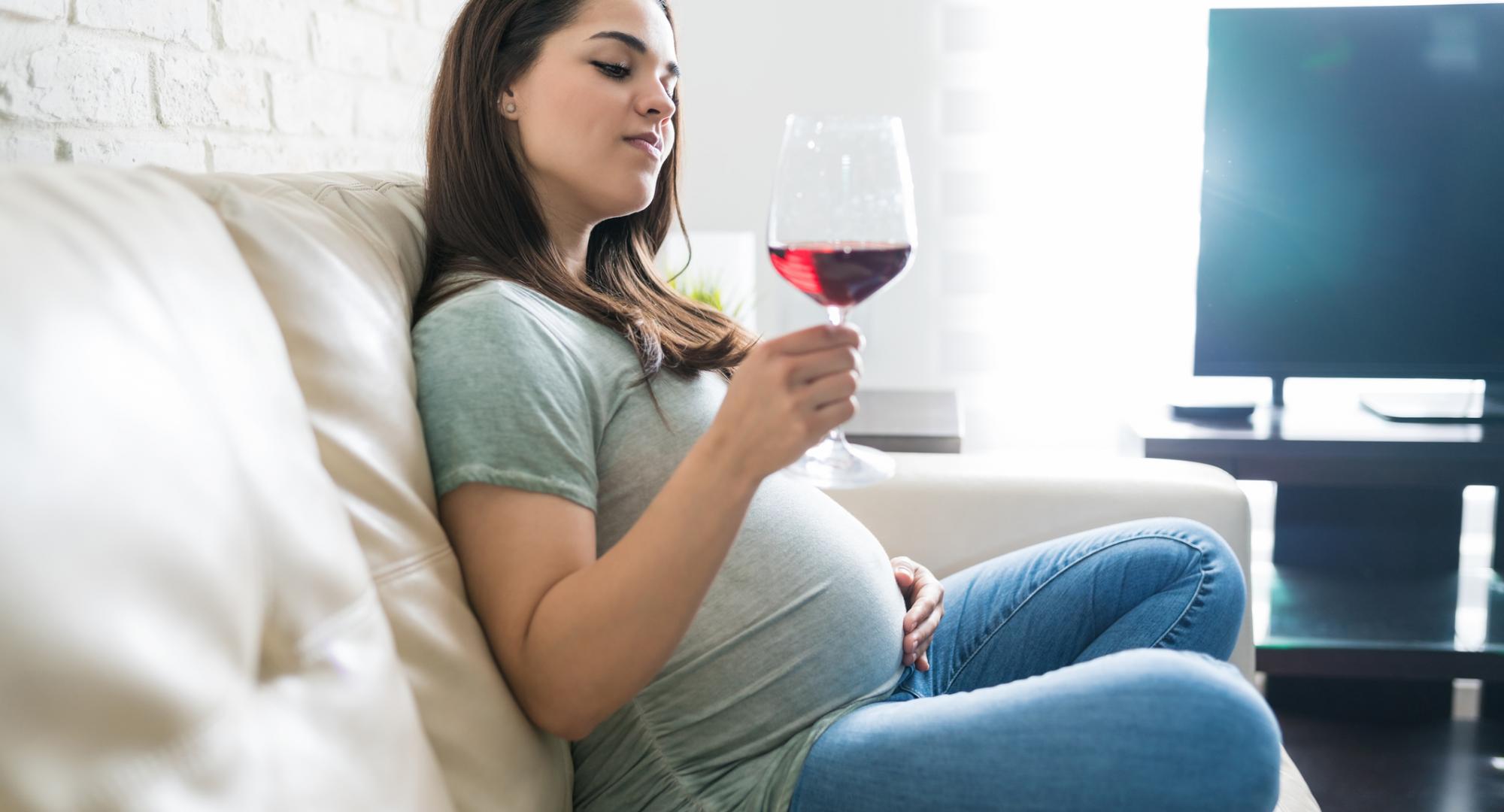 Pregnant woman enjoys glass of wine at home.