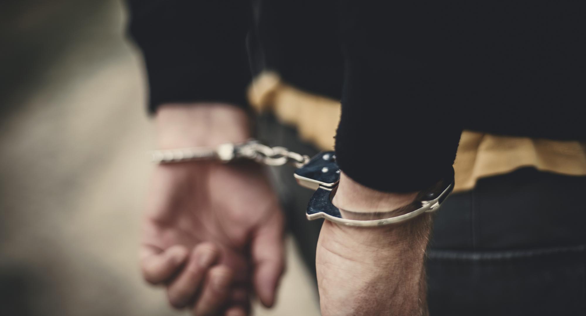 Man with arms behind his back in handcuffs.