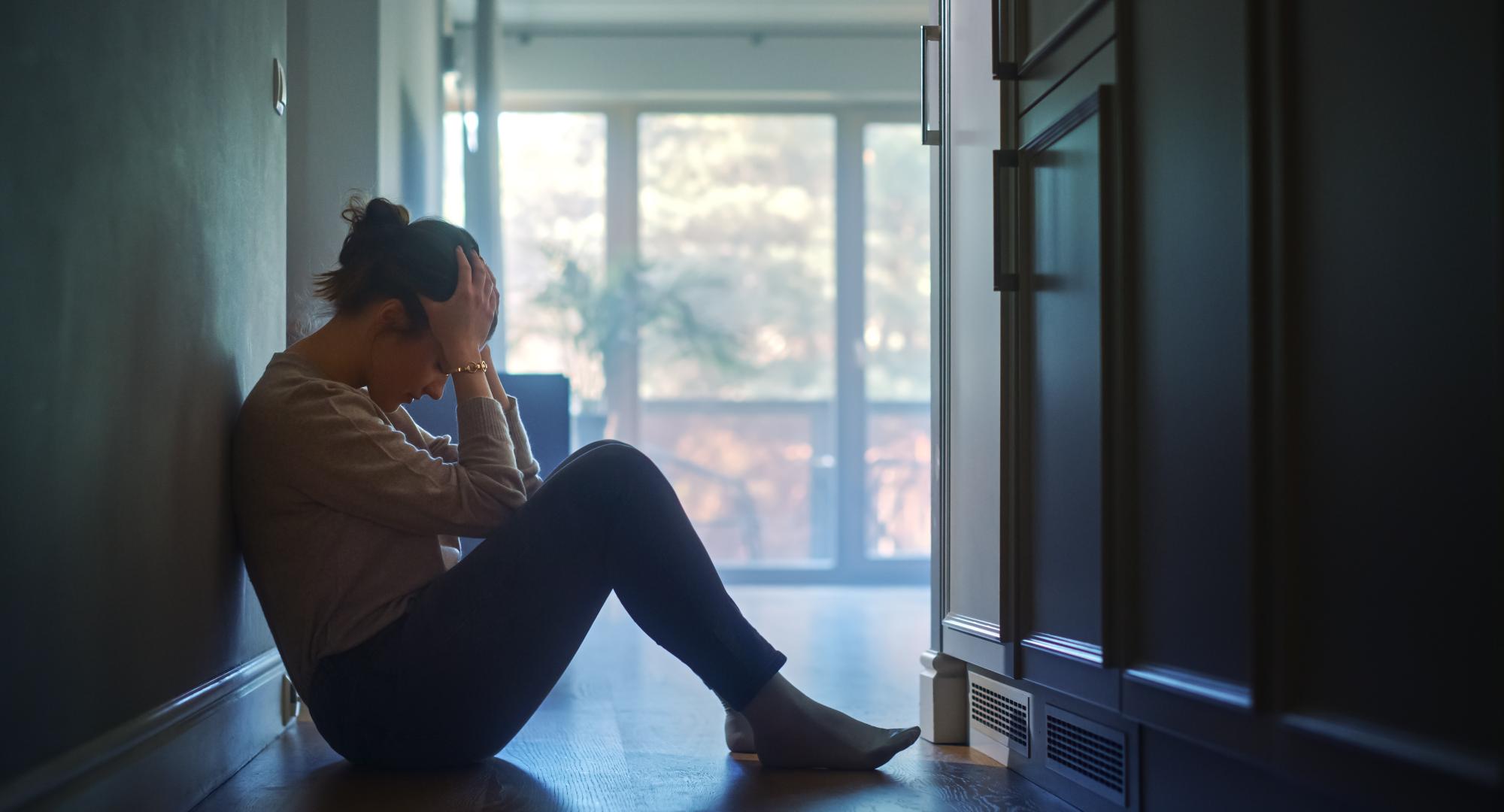 A woman sits in the hallway of her home with her head in her hands.