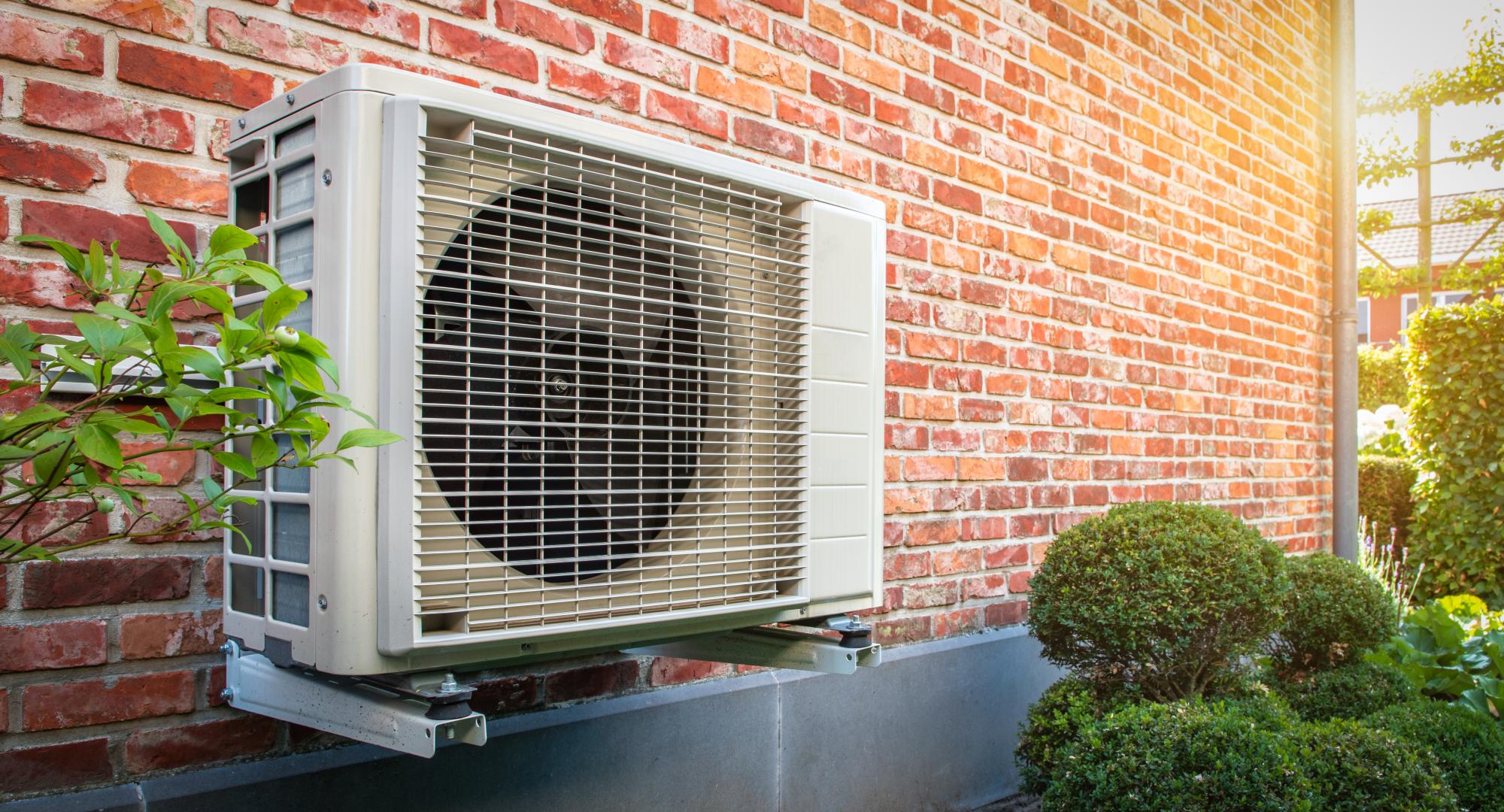 Heat pump outside a home, against a brick wall