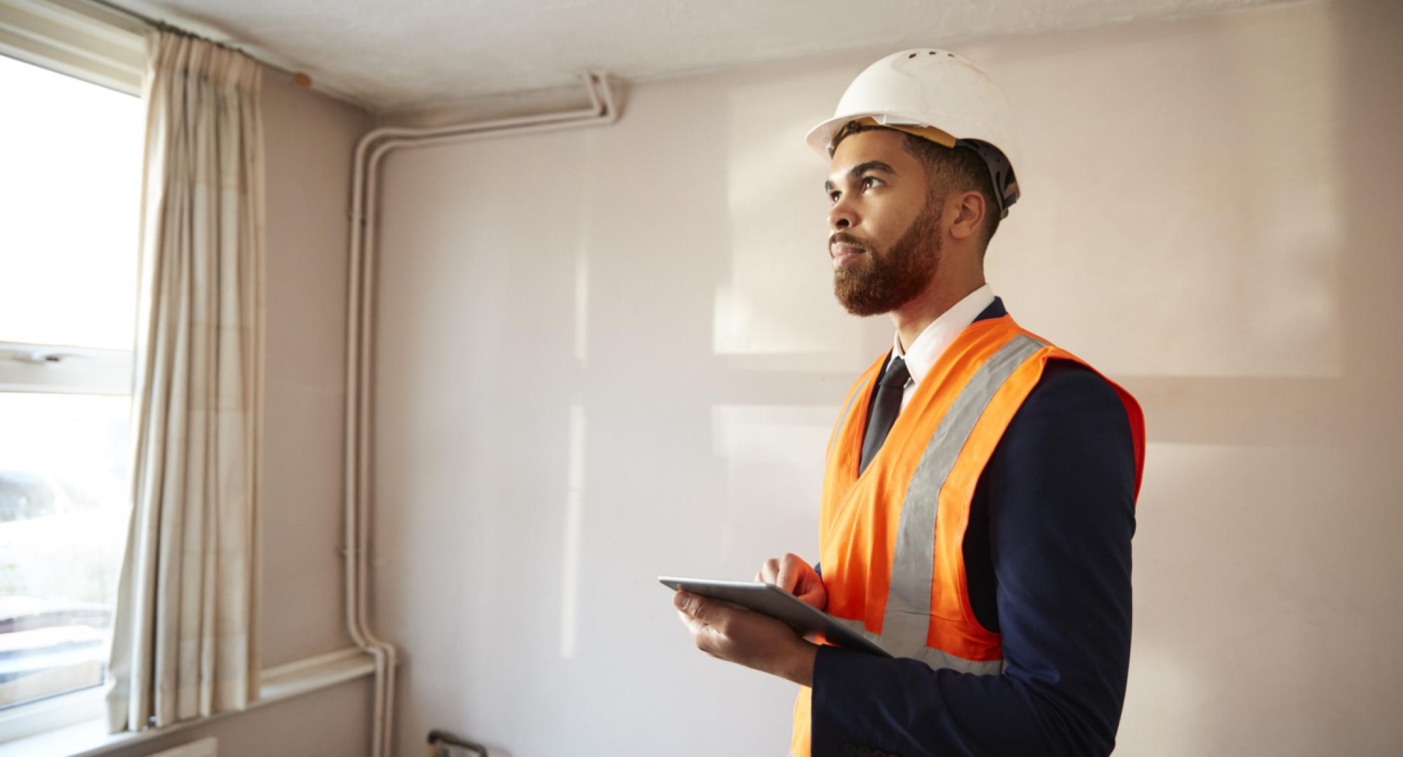 Surveyor In Hard Hat And High Visibility Jacket With Digital Tablet Carrying Out House Inspection