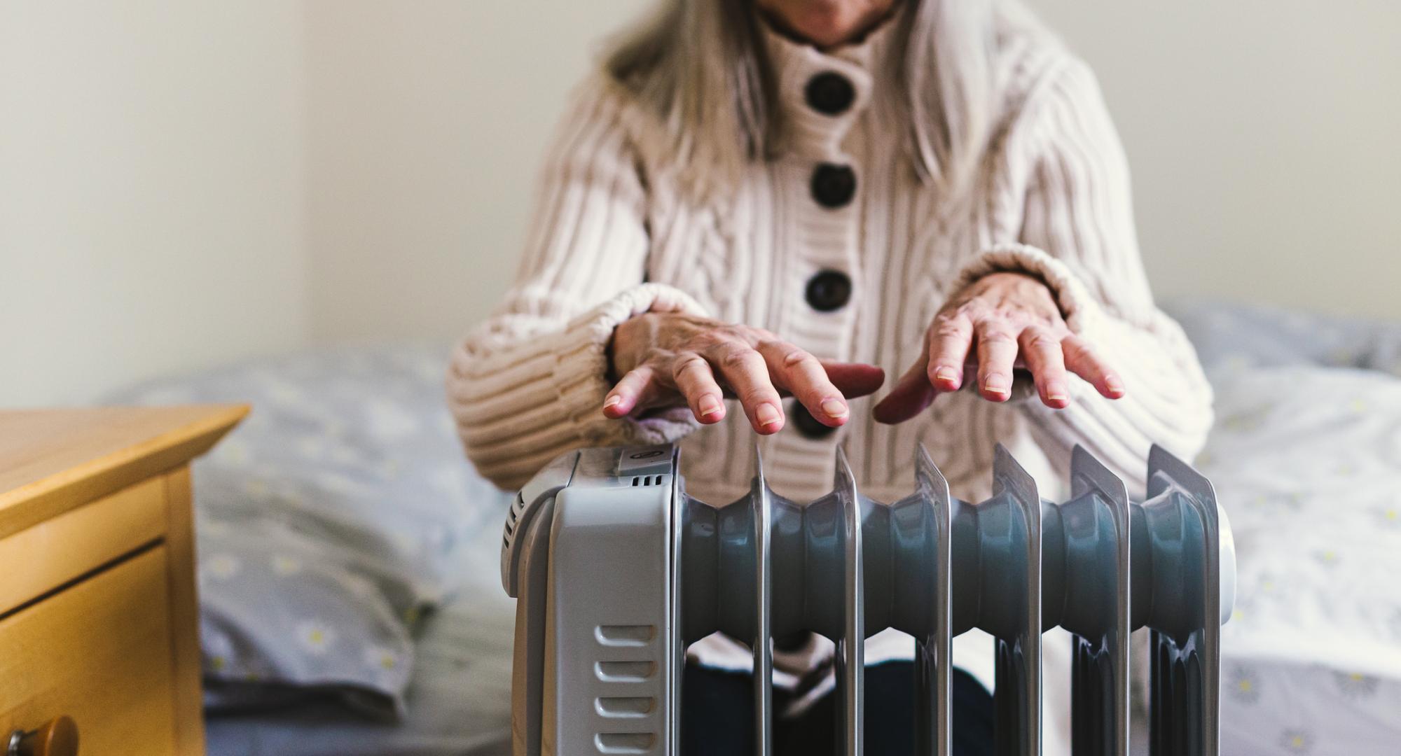 A pensioner sits in her cold home, next to a space heater