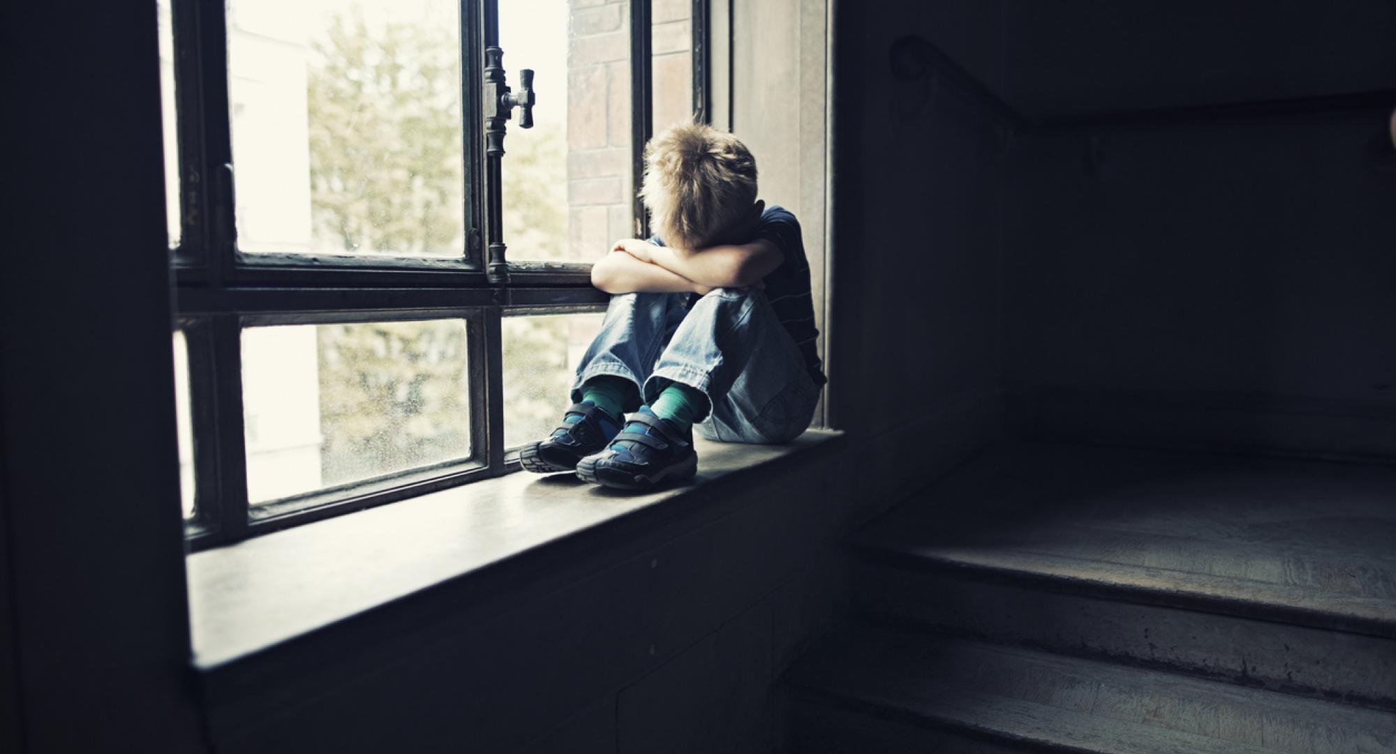 Depressed child sitting on window