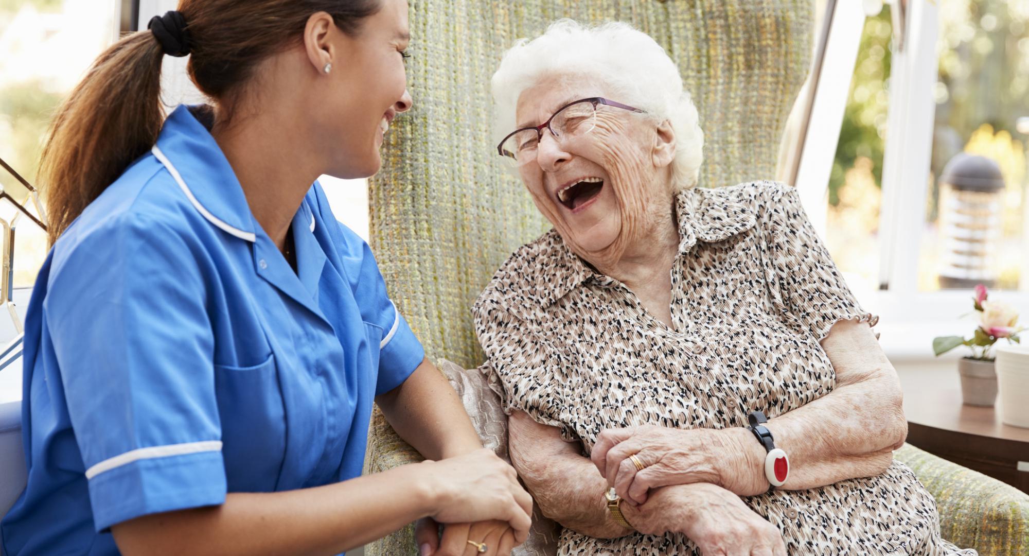 Senior Woman Sitting In Chair And Laughing With Nurse