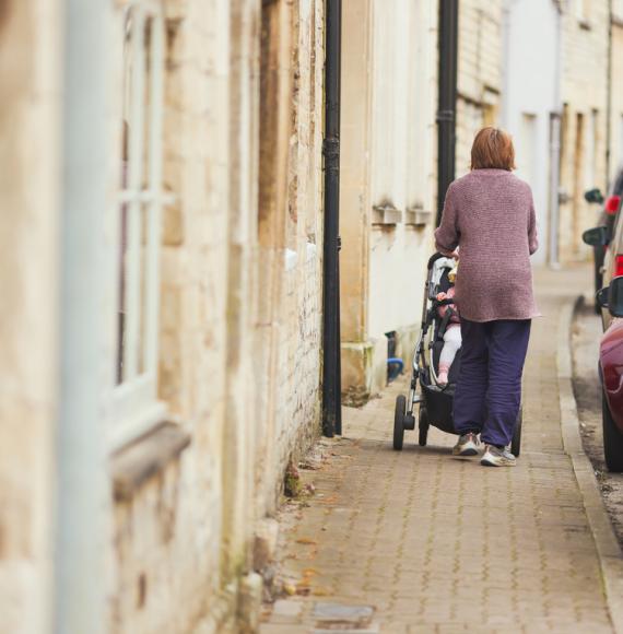 Woman pushing a child along the pavement in a pushchair